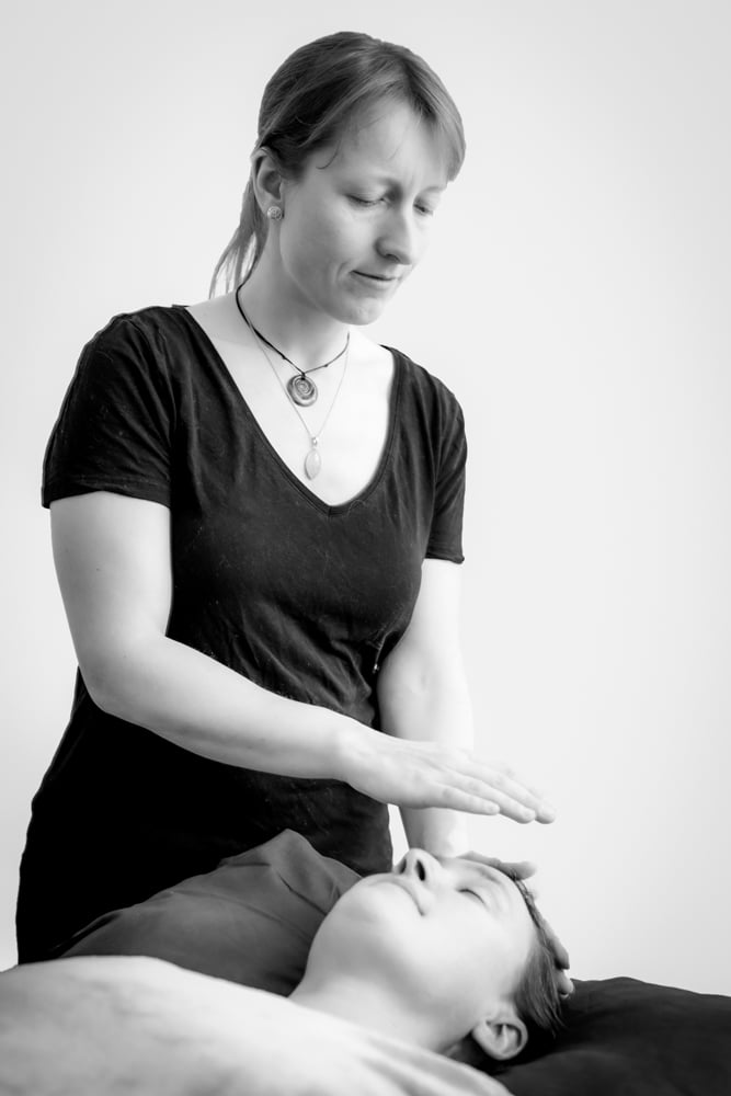 Reiki treatment being given by Jen Grange of Lakeland Wellbeing to a lady lying down on a therapy bed.
