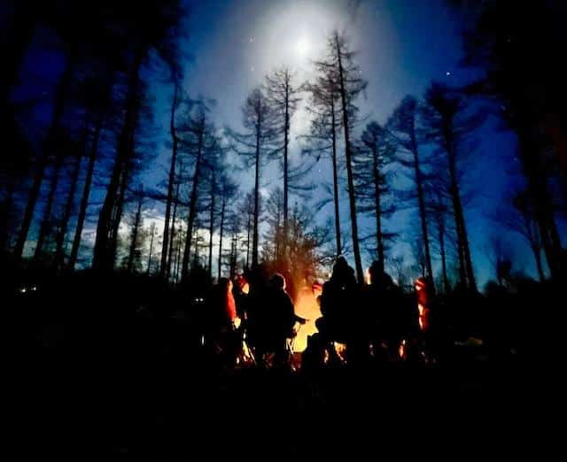 Full Moon Women's Circle being held in a forest with women sitting in a circle around a ceremonial fire.